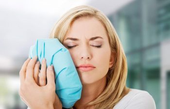 Woman with dental pain pressing a cold compress to her cheek.