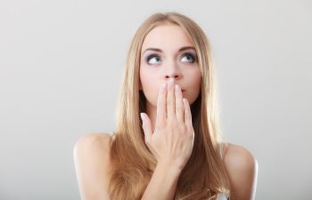 A young woman covering her mouth with her hand because of bad breath.