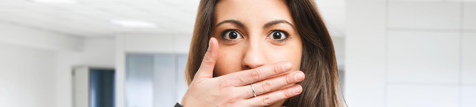 A young woman covering her mouth with her hand due to bad breath.