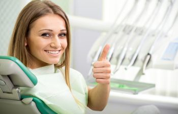 A satisfied young woman in a dental chair showing her thumb up.